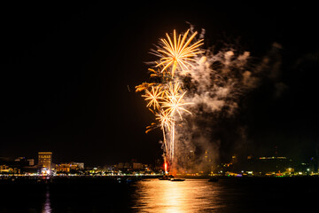 Brilliant red fireworks explode against a dark night sky, illuminating a cityscape below. Vibrant...
