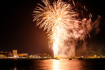 Brilliant red fireworks explode against a dark night sky, illuminating a cityscape below. Vibrant...