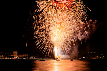Brilliant red fireworks explode against a dark night sky, illuminating a cityscape below. Vibrant...