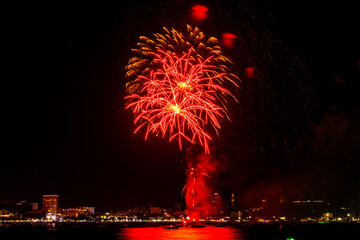 Brilliant red fireworks explode against a dark night sky, illuminating a cityscape below. Vibrant...
