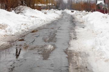 A road is covered in snow and has puddles of water on it