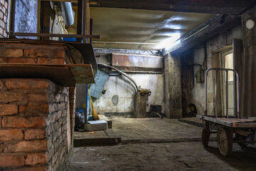 Dimly lit industrial room with exposed brick walls, aged concrete floors, metal pipes, and a cart. The gritty space reflects an atmosphere of abandonment and urban decay, highlighting its character
