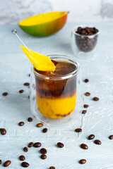 A glass of iced coffee with mango juice and coffee beans on a table