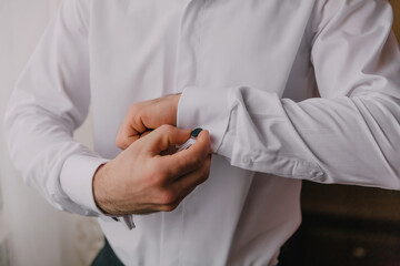 A man is getting dressed in a white shirt and is adjusting his cuff. Concept of formality and attention to detail, as the man takes care to properly dress himself