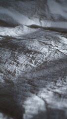 Textured white sheets in the bedroom with morning sunlight. Messy bed after night sleep concept. Rumpled bed sheet and duvet textile. Fabric and linen background.