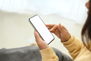 Woman in yellow sweater holding smartphone with white empty display sitting on sofa