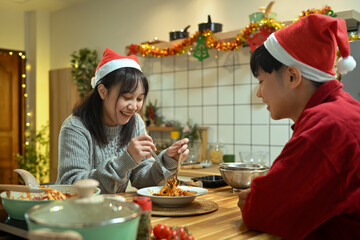 Loving young couple in Santa hats enjoying Christmas dinner together in cozy kitchen