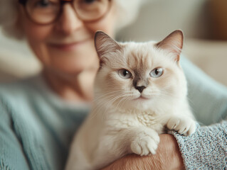 Obraz premium Elderly Cat Love Concept. An elderly woman smiles while holding a fluffy white cat, showcasing a moment of companionship and warmth between them.