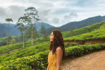 A serene woman in a yellow dress admires the beauty of lush tea plantations in Nuwara Eliya, Sri Lanka. The peaceful green hills and mountain backdrop create a perfect setting for travel, nature, and