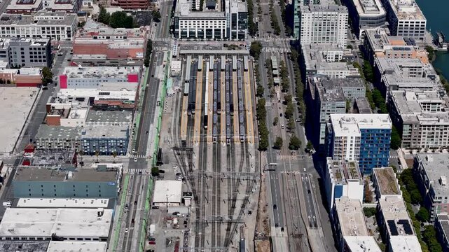 A fly-down aerial view of the Caltrain station in San Francisco, capturing the organized train tracks, parked trains, surrounding roads, and nearby buildings.