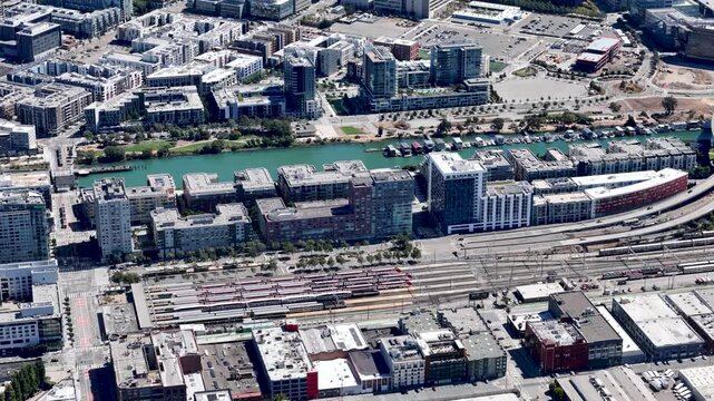 A rotating aerial view of the Caltrain station in San Francisco Mission Bay area, capturing the station, nearby residential complexes, and the adjacent canal.