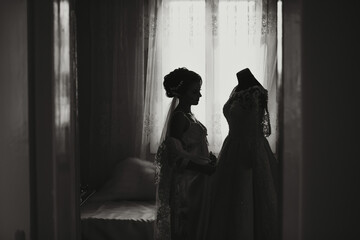 A woman is standing in front of a dresser with a white wedding dress on it. She is likely getting...