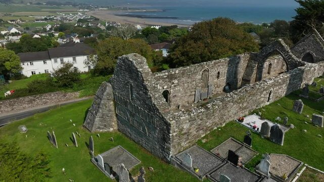 St. Declan's Monastery, Ardmore, County Waterford, Ireland, September 2024. Drone pulls back and orbits clockwise over the stone ruin of the 12th century Cathedral with North Atlantic in the distance.