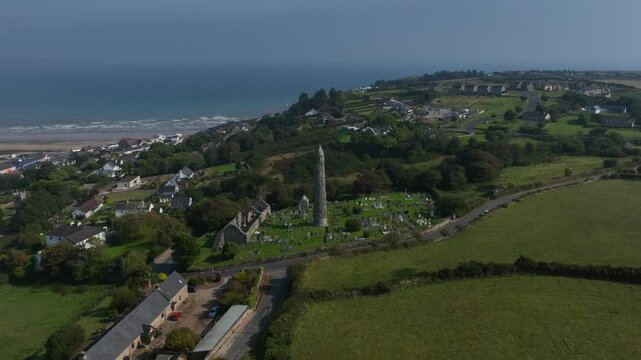 St. Declan's Monastery, Ardmore, County Waterford, Ireland, September 2024. Drone orbits counter clockwise pulling backward around the Round Tower as waves crash and roll towards the distant beach.