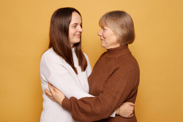 Two women embrace with warm smiles against a vibrant yellow background, showcasing a moment of connection and affection in a studio setting, emphasizing their emotional bond