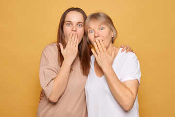 Two women with surprised expressions covering their mouths against a vibrant yellow backdrop,...