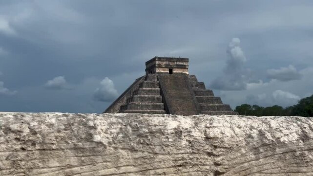 Handheld booming up shot over a stone wall to reveal the ancient Mayan pyramid El Castillo in Chichen Itza, Mexico. 4K
