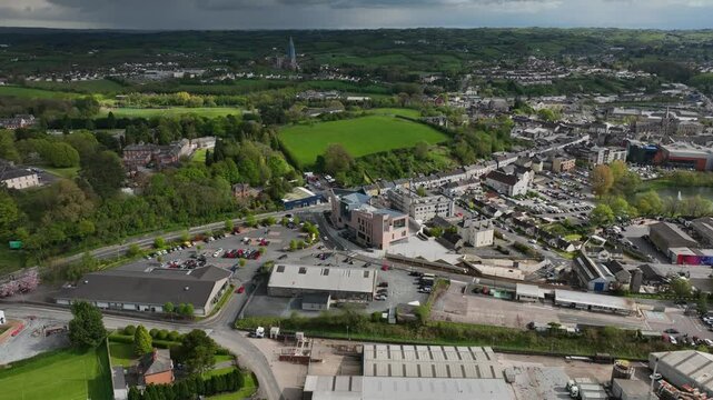 Peace Campus, County Monaghan, Ireland, April 2024. Drone orbits clockwise around Monaghan County Museum surrounded by green fields and trees under a cloudy sky with Patena Lake in the distance.