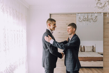 Two men in suits shaking hands in front of a mirror. Scene is professional and formal