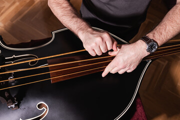 Top view of a man's hands pulling the E string (fourth string) to adjust the tension on a ¾ double...