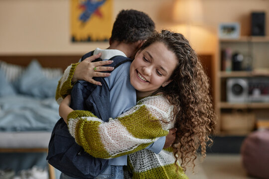 Portrait shot of smiling adoptive mother giving tender hug to Black boy in bedroom raising happy confident kid while sending son off to school, copy space