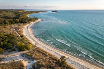 Luftaufnahme eines einsamen Sandstrandes mit grüner Küstenlinie und klarem Wasser bei Sonnenuntergang.