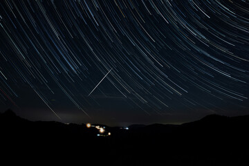 Star trails of a Milky Way with meteor, shooting stars and countryside silhouettes.