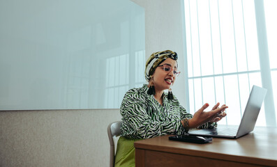Indian businesswoman in creative workspace participating in a virtual meeting with enthusiasm