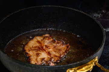 Sizzling pork chop frying in a cast iron skillet with golden edges in a cozy kitchen setting