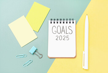 The inscription goals 2025 on notepad on yellow and green background, top view.