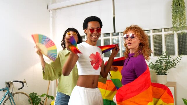 Gay man with lesbian woman friends celebrating pride dancing waving lgbt rainbow flag