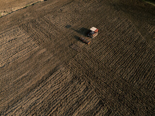 Red tractor plowing a cultivated field, preparing the land for sowing, creating furrows in the fertile soil.