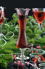 Christmas or New Year's red drinks in glasses decorated with green ornaments and Christmas twigs; bokeh, black background.