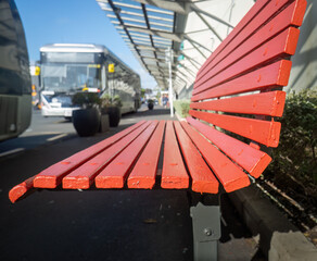 Empty red bench at the bus stop. Out-of-focus buses along the road. Auckland.
