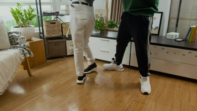Tilt up shot of young bi-ethnic couple in casualwear performing contemporary dance moves in living room