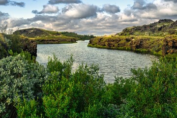 Tranquil river with lush greenery and rocky hills.