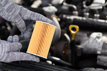 Man in gloves holds diesel car oil filter with both hands against background of engine compartment,...