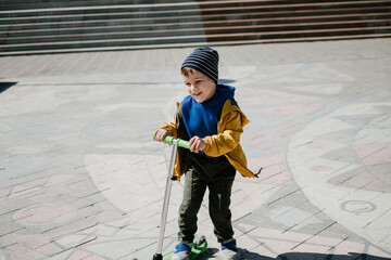 A little boy rides a scooter outdoors in an urban environment.