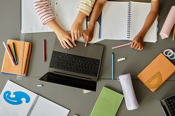 Top view of two unrecognizable young students using laptop together keeping fingers on touchpad...
