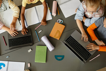 Top view of unrecognizable primary school children working in pairs using laptops to study in class...