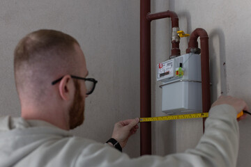 Man measuring the distance between gas pipes of gas meter at home with measuring tape.
