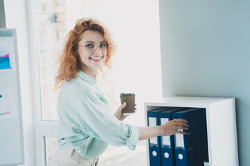 Portrait of young business woman hold coffee take folder shelf wear shirt modern interior office indoors