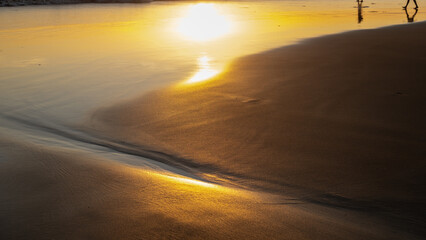 Golden sunlight reflecting on wet sand at sunset, creating a serene and peaceful beach scene with smooth, flowing textures. A tranquil coastal moment.