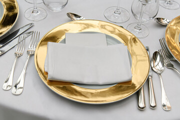 Luxurious table setting featuring gold charger plates, silverware, and a folded white napkin. Perfect for weddings, fine dining, and formal events, showcasing elegance and sophistication.