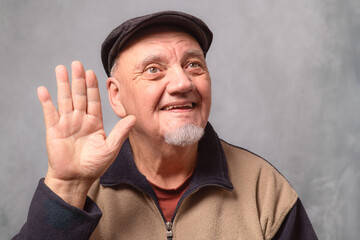 portrait homme sénior avec béret main en avant fond gris