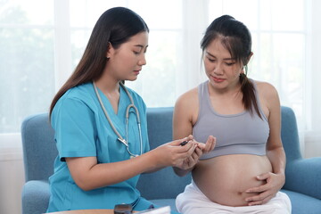 Asian female doctor uses medical equipment to listen to the baby's heartbeat in the womb, draws blood to check blood sugar and take care of the health of a pregnant woman at a clinic.