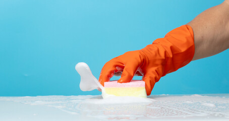 Hand in orange rubber glove hold cleaning brush sponge and wipe soap foam bubble splash in air over...