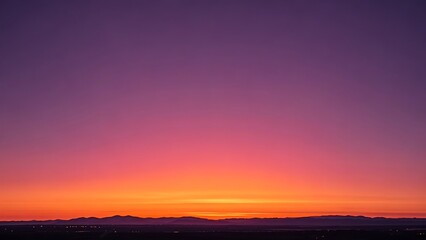 Fototapeta premium A vibrant, colorful sunset with a gradient of orange, pink, and purple hues over a distant mountain range.