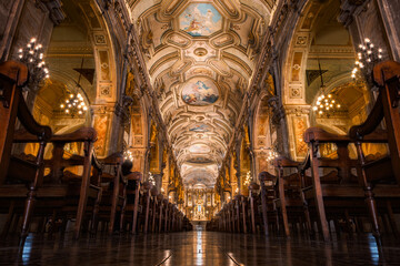 The main nave of the Santiago Metropolitan Cathedral in Santiago, Chile. It features grand columns topped with wooden statues of apostles and a beautifully painted ceiling decorated with ornate detail