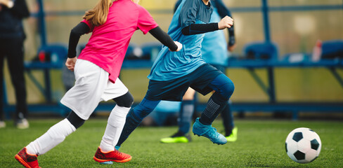 School Boy and Girl In Soccer Teams Competing For The Ball During A Football Match. Kids Play Sports In Front of Soccer Bench. Happy Children Play Soccer Ball on Grass Pitch